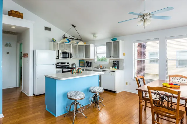 a kitchen with stainless steel appliances a stove a refrigerator a sink a dining table and chairs with wooden floor