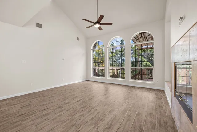 an empty room with wooden floor fan and windows