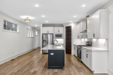 a large kitchen with stainless steel appliances kitchen island granite countertop a refrigerator oven a sink dishwasher and white cabinets with wooden floor