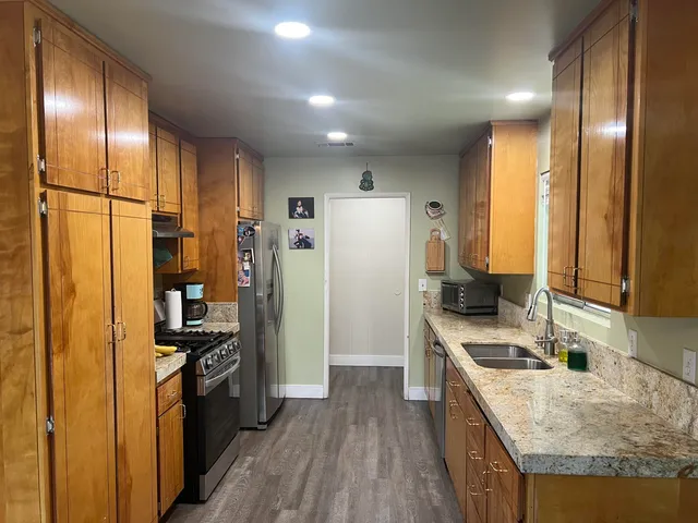 a kitchen with stainless steel appliances granite countertop a refrigerator a stove and a sink with wooden floor