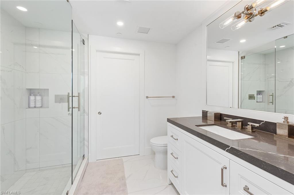 13945 Old Coast Road, Unit 406 Naples, FL 34110 - Photo 21 of 46 a bathroom with a granite countertop sink a toilet a large mirror and shower
