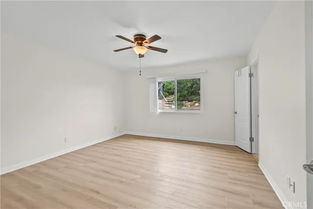 an empty room with wooden floor chandelier fan and windows