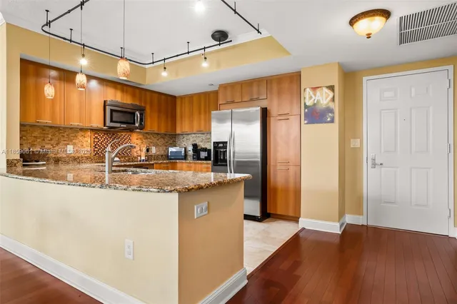 a kitchen with granite countertop a refrigerator a sink a stove a microwave and wooden floors