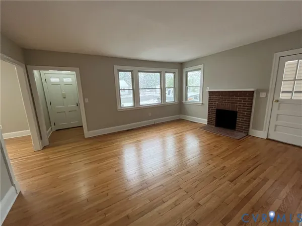 an empty room with wooden floor fireplace and windows