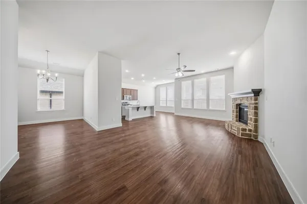 an empty room with wooden floor and kitchen view