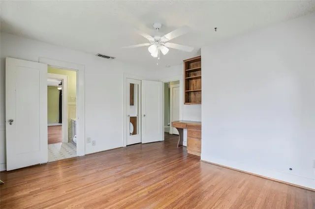 a view of an empty room with wooden floor and a ceiling fan