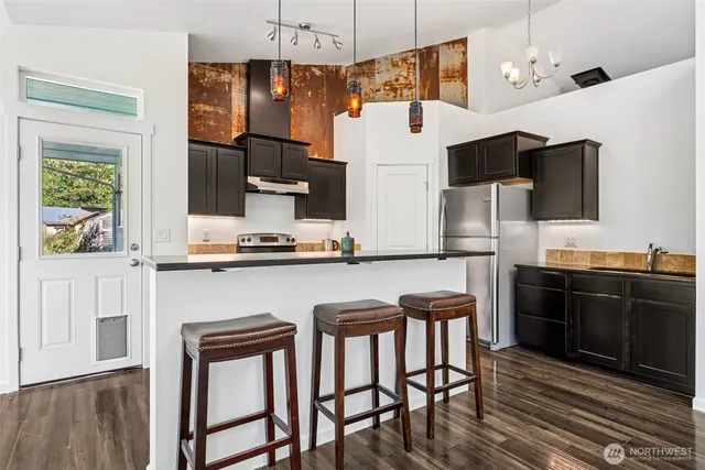 a kitchen with stainless steel appliances kitchen island granite countertop a refrigerator a stove and white cabinets with wooden floor