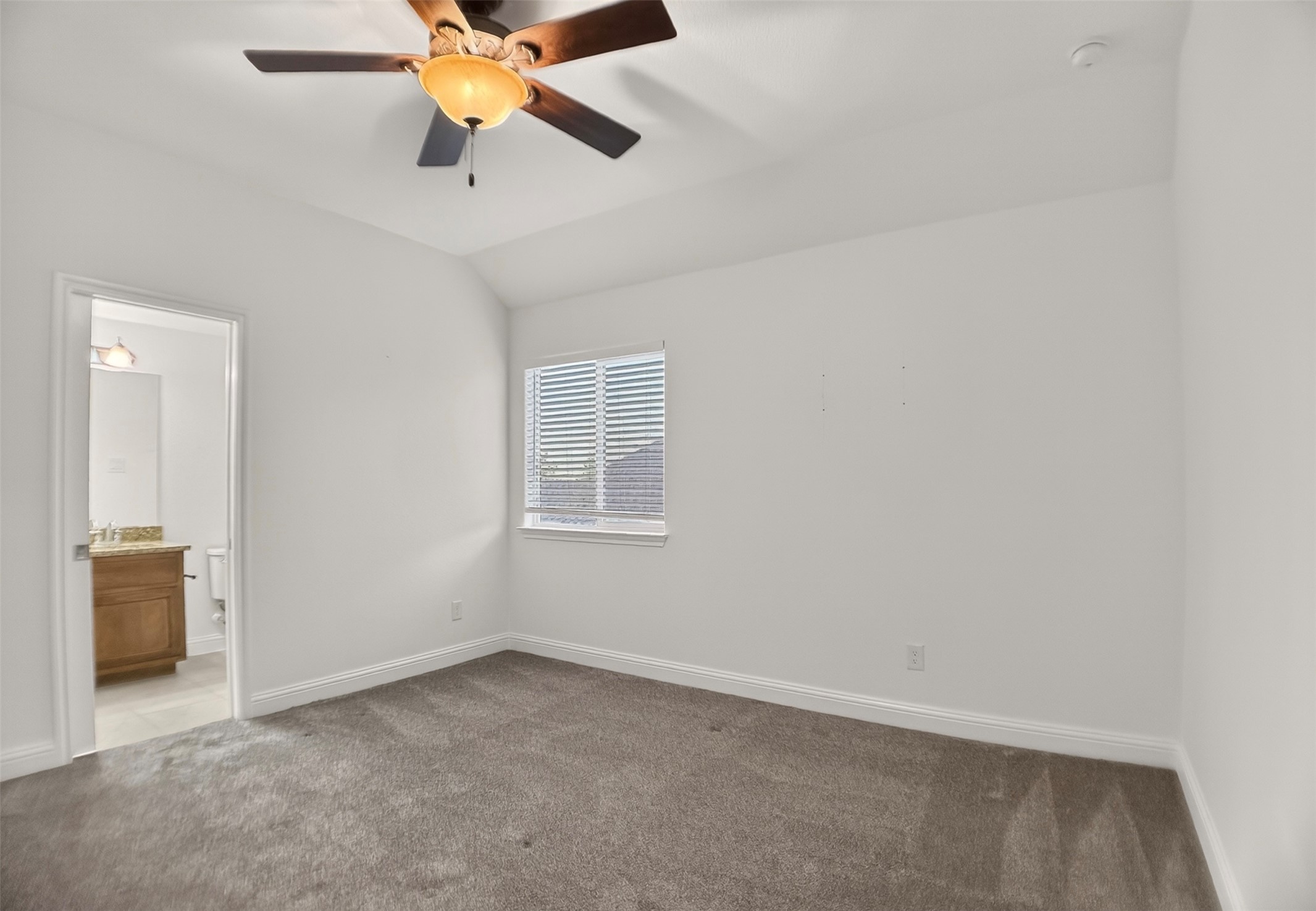 1505 Long Shadow Lane Georgetown, TX 78628 - Photo 20 of 28 Carpeted room featuring a ceiling fan with light fixture, a window with horizontal blinds, and a doorway revealing a bathroom with a wood-finish vanity and stone-look countertop
