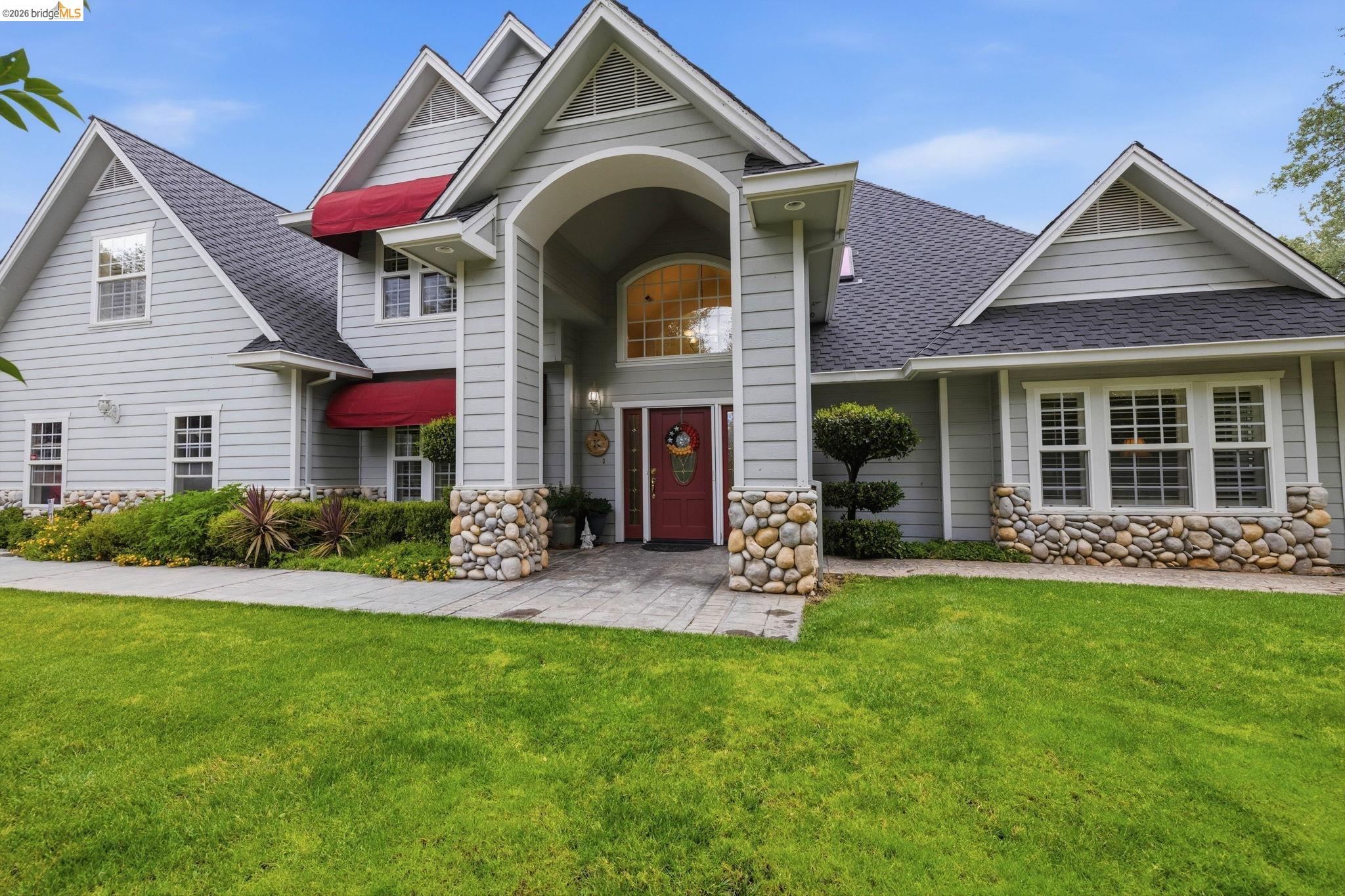 18450 Lambert Lake Road Sonora, CA 95370 - Photo 4 of 87 Light grey siding exterior featuring red awnings and a prominent arched entryway