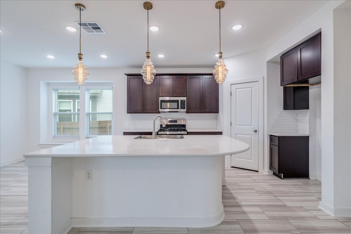 8008 Prairie Rye Drive Lago Vista, TX 78645 - Photo 21 of 40 Kitchen featuring a curved central island with white countertop, dark wood-finish cabinetry, stainless steel appliances, and a tiled backsplash