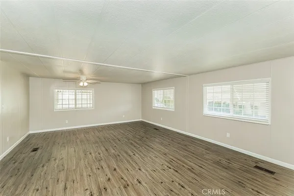 an empty room with wooden floor fan and windows