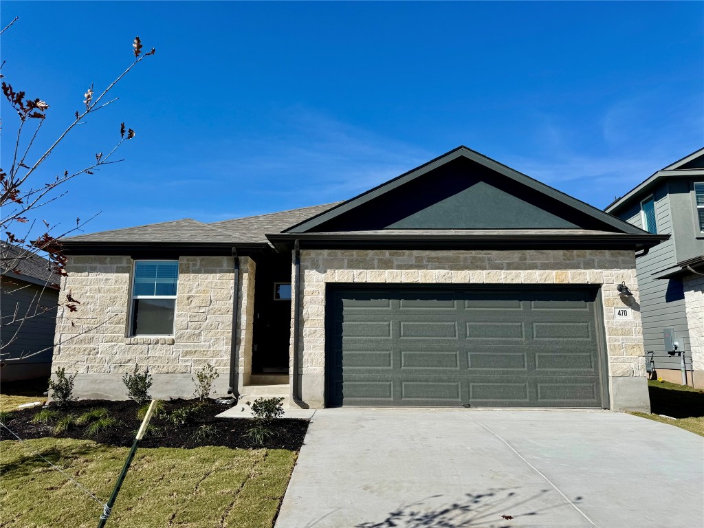 View of front facade featuring stone siding, driveway, and an attached garage