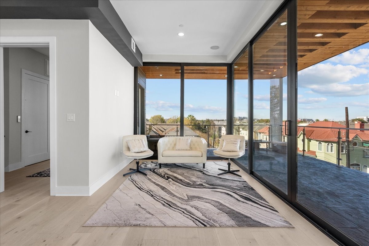 516 Reinerman Street Houston, TX 77007 - Photo 33 of 42 Modern living area with floor-to-ceiling windows offering abundant natural light and city views. Features elegant light wood flooring, a stylish rug, and cozy seating, leading to a spacious balcony.