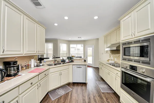 a kitchen with stainless steel appliances a sink dishwasher a stove top oven a refrigerator with white cabinets and wooden floor