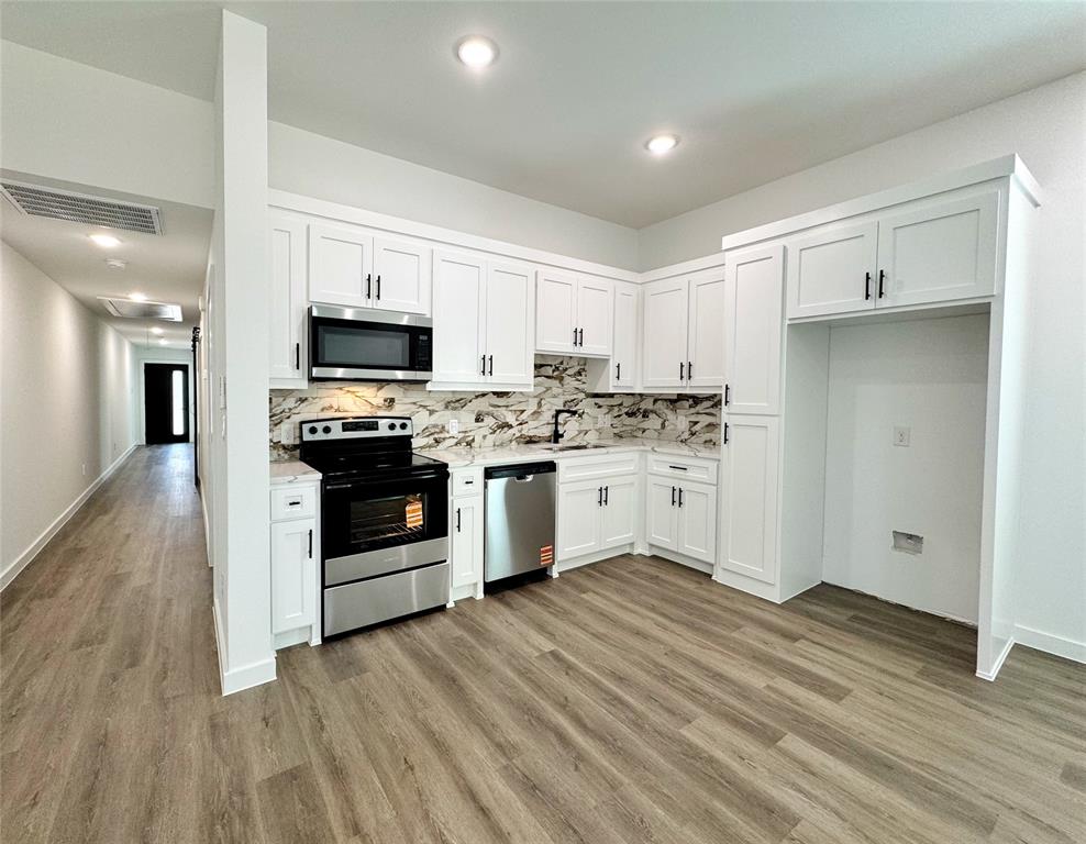 1811 Washington Street Commerce, TX 75428 - Photo 21 of 36 a kitchen with stainless steel appliances a white stove top oven cabinets and a wooden floor