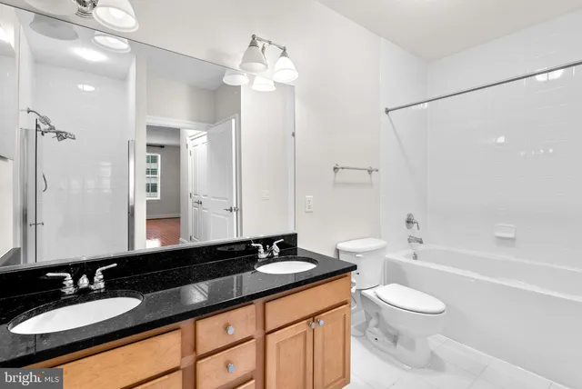 a bathroom with a granite countertop sink a toilet a mirror a bathtub and shower