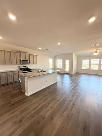 a kitchen with granite countertop a stove top oven a sink and white cabinets with wooden floor