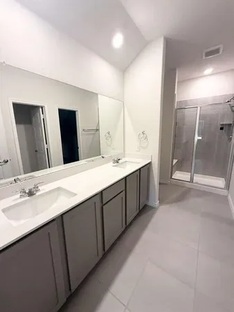 a spacious bathroom with a double vanity sink a large mirror and shower