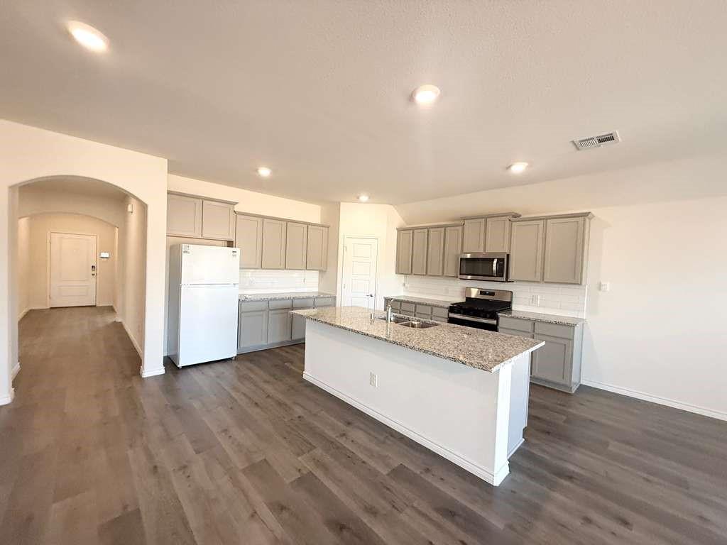 804 Marigold Street Princeton, TX 75407 - Photo 9 of 19 Kitchen with arched walkways, gray cabinetry, stainless steel appliances, an island with sink, and light stone countertops