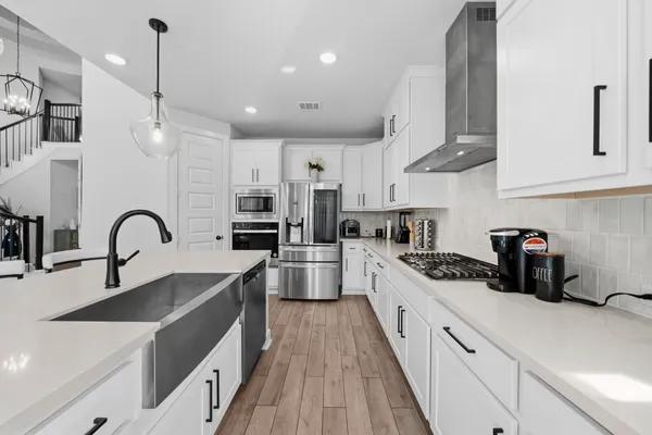 a white kitchen with stainless steel appliances granite countertop a sink a stove and a wooden floors