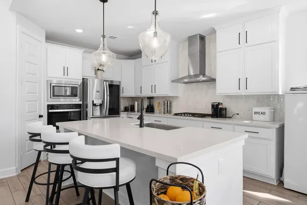 a kitchen with stainless steel appliances a stove a refrigerator a sink a dining table and chairs with white cabinets