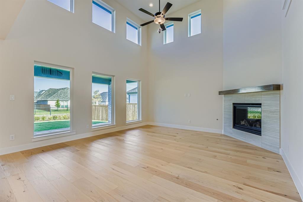3324 Little Bluestem Road Celina, TX 75009 - Photo 6 of 29 Unfurnished living room with a tile fireplace, light wood-type flooring, ceiling fan, and a high ceiling