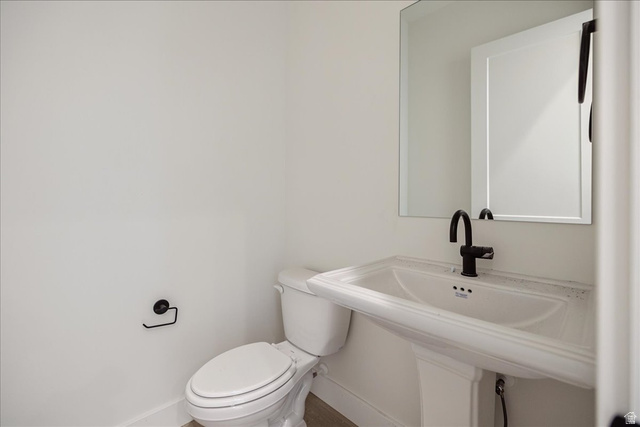 7189 South Sage Road, Unit 214 West Jordan, UT 84081 - Photo 11 of 29 Pedestal sink with a matte black faucet, wall-mounted mirror, and white toilet