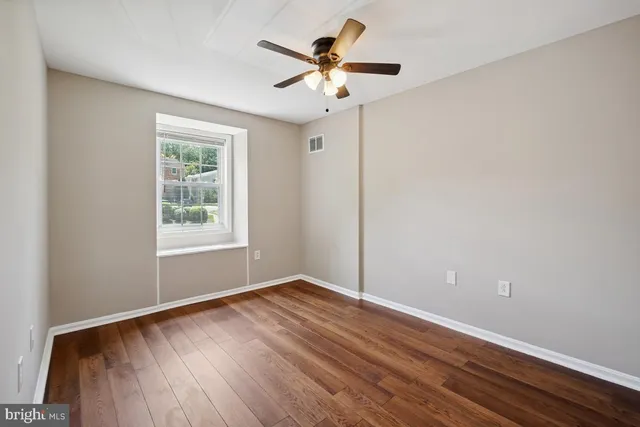 an empty room with wooden floor chandelier fan and windows