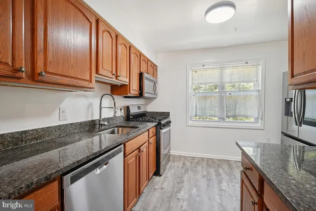 a kitchen with granite countertop stainless steel appliances a sink window and cabinets