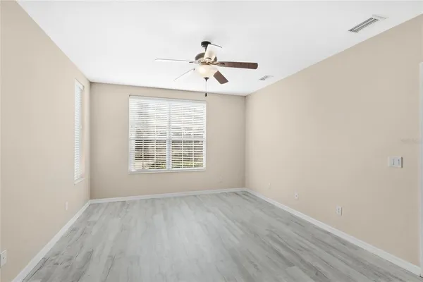 an empty room with wooden floor chandelier fan and windows