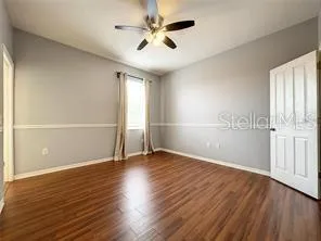 an empty room with wooden floor fan and windows