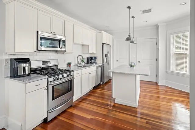 a kitchen with stainless steel appliances white cabinets a sink a stove a microwave and wooden floors