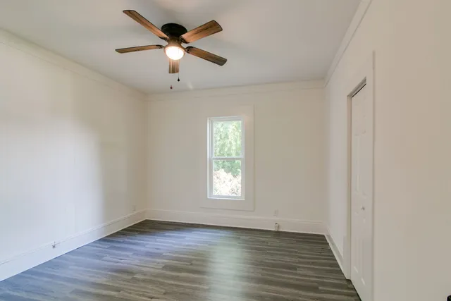 an empty room with wooden floor ceiling fan and window