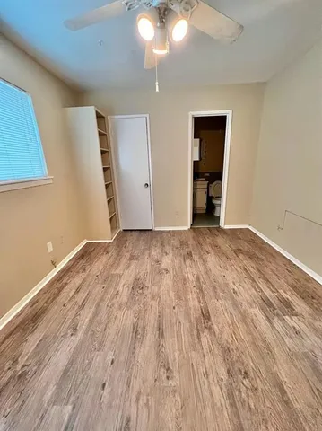 a view of an empty room with wooden floor and a ceiling fan