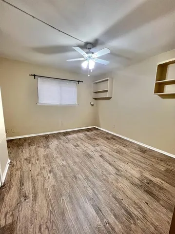 a view of an empty room with wooden floor and a ceiling fan