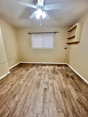 a view of an empty room with wooden floor and a ceiling fan