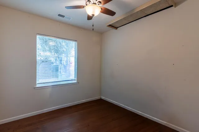 an empty room with wooden floor chandelier fan and windows