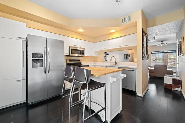 a kitchen with stainless steel appliances kitchen island granite countertop a refrigerator a sink a stove and white cabinets with wooden floor