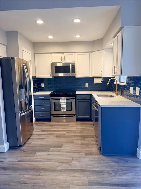 14333 Preston Road, Unit 806 Dallas, TX 75254 - Photo 9 of 17 Stainless steel appliances, white upper cabinetry, blue lower cabinetry, blue subway tile backsplash, and light-toned wood-finish flooring