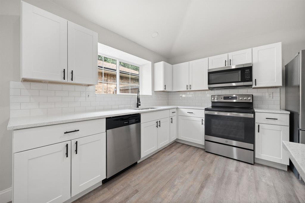 310 Valley Spring Drive Arlington, TX 76018 - Photo 7 of 24 Kitchen featuring white shaker-style cabinetry, stainless steel appliances, a white subway tile backsplash, and light-toned wood-finish flooring