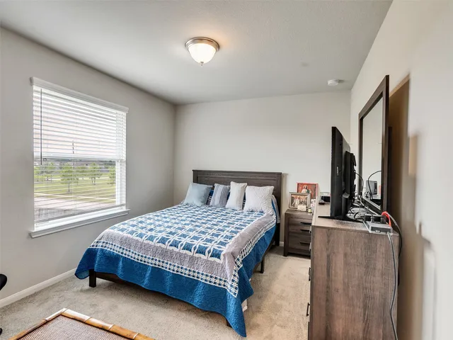 a bedroom with a bed table flat screen tv and a window