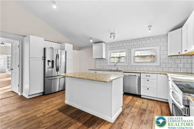 a kitchen with granite countertop a refrigerator oven a sink dishwasher and white cabinets with wooden floor