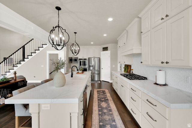1132 South 1300th Street West Mapleton, UT 84664 - Photo 11 of 52 Open-concept kitchen featuring an expansive island with a waterfall-edge countertop, white shaker-style cabinetry, stainless steel appliances, a five-burner gas cooktop, and wood-finish flooring