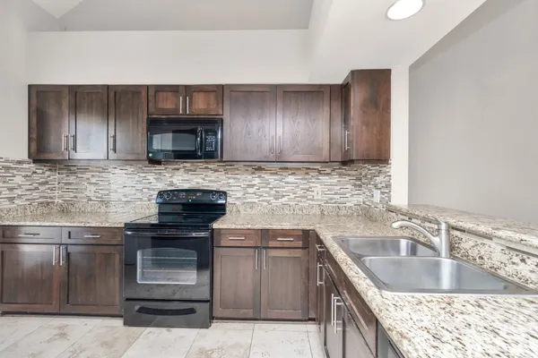 a kitchen with granite countertop a sink and a stove top oven with wooden cabinets
