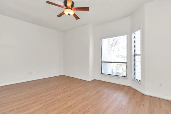 an empty room with wooden floor fan and windows