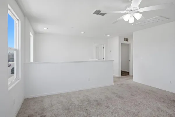 an empty room with a ceiling fan and kitchen view