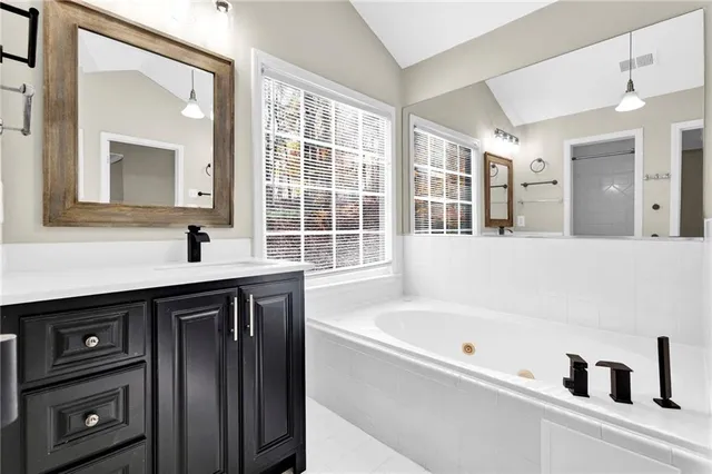 a bathroom with a bathtub a sink a vanity a window and a mirror