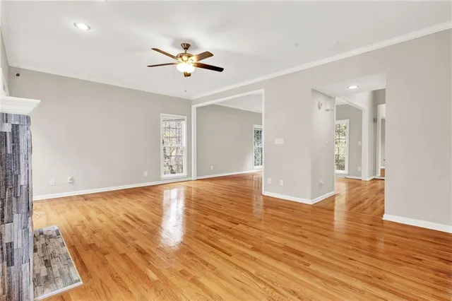 a view of an empty room with wooden floor and a ceiling fan