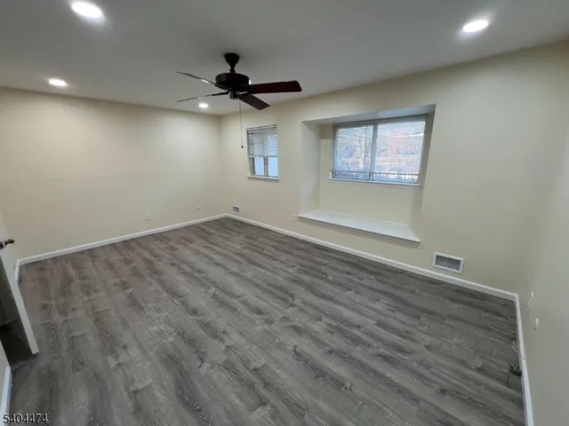 an empty room with wooden floor ceiling fan and windows