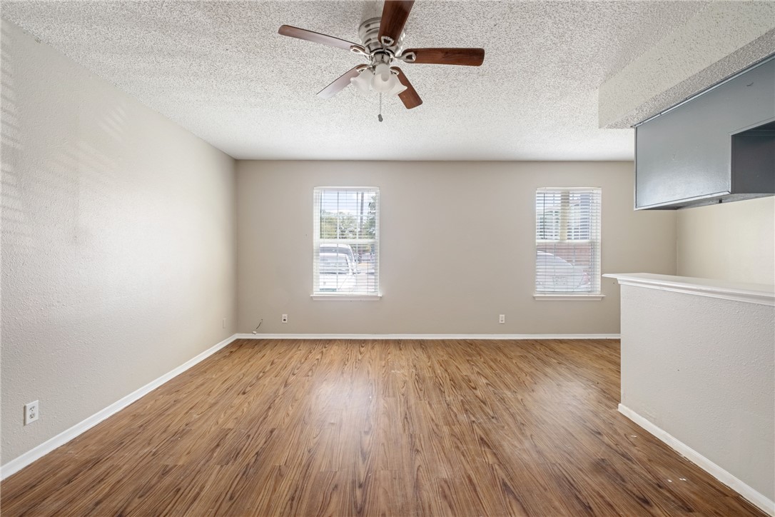 an empty room with wooden floor a ceiling fan white walls and windows